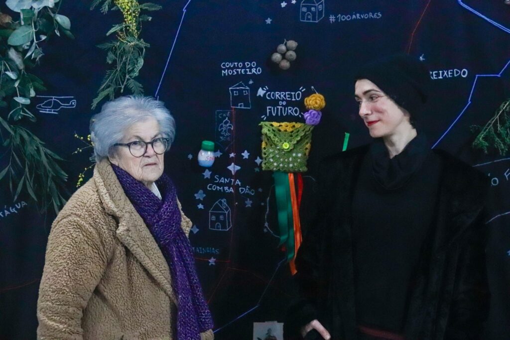 An older lady and a young artist pose in front of the canvas